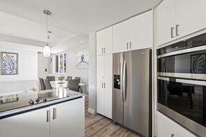 Una cocina moderna con electrodomésticos de acero inoxidable, armarios blancos y una isla central con asientos.