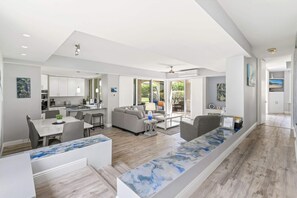 A spacious living area with a kitchen, dining space, and a large window providing a view of the outdoors. - The Palms at Wailea (Kihei)