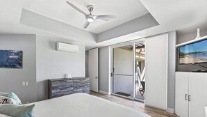 A bedroom with a bed, a ceiling fan, a TV, and a sliding glass door leading to a balcony. - The Palms at Wailea (Kihei)