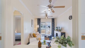 A modern living room with a ceiling fan, a dining table with a colorful sculpture, and a potted plant. - cozy Ground-floor apartment 4p terrace pool & parking beach --> 2km (VC)