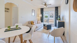 A modern living room with a white sofa, a dining table with chairs, and two ceiling fans. - cozy Ground-floor apartment 4p terrace pool & parking beach --> 2km (VC)