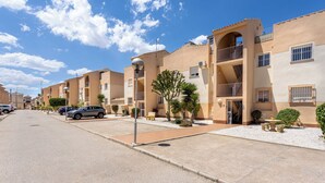 Una hilera de edificios de apartamentos modernos con balcones, cielo despejado y zona de estacionamiento.