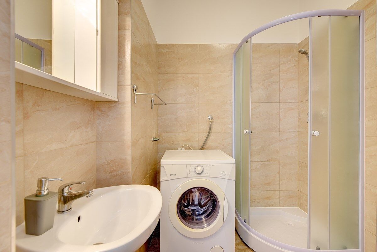 A compact bathroom with a sink, washing machine, and a glass-enclosed shower.