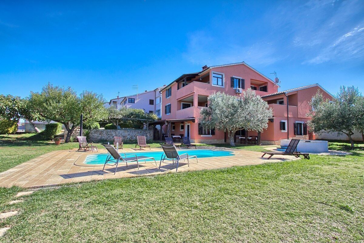 A two-story building with a swimming pool, outdoor seating, and a well-maintained lawn.