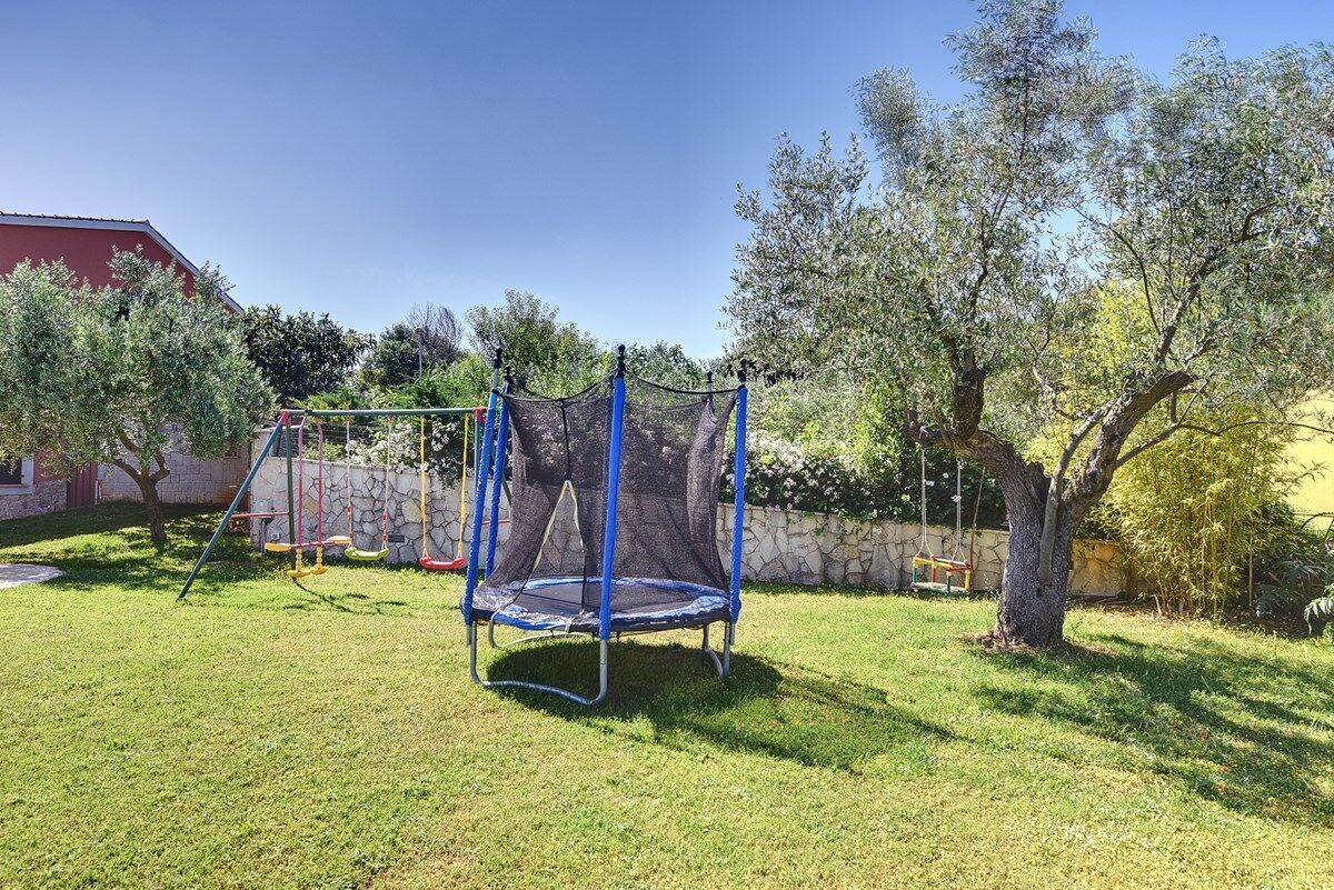 En baghave med trampolin, gyngestativ og et træ.