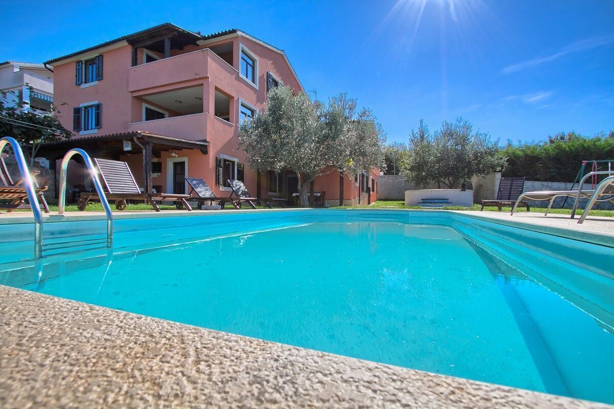 Una piscina con sillones de descanso y un edificio al fondo.