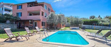 A swimming pool with lounge chairs, a pink building, and a clear blue sky.