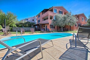 Une piscine avec des chaises longues et, au fond, un bâtiment doté de balcons.