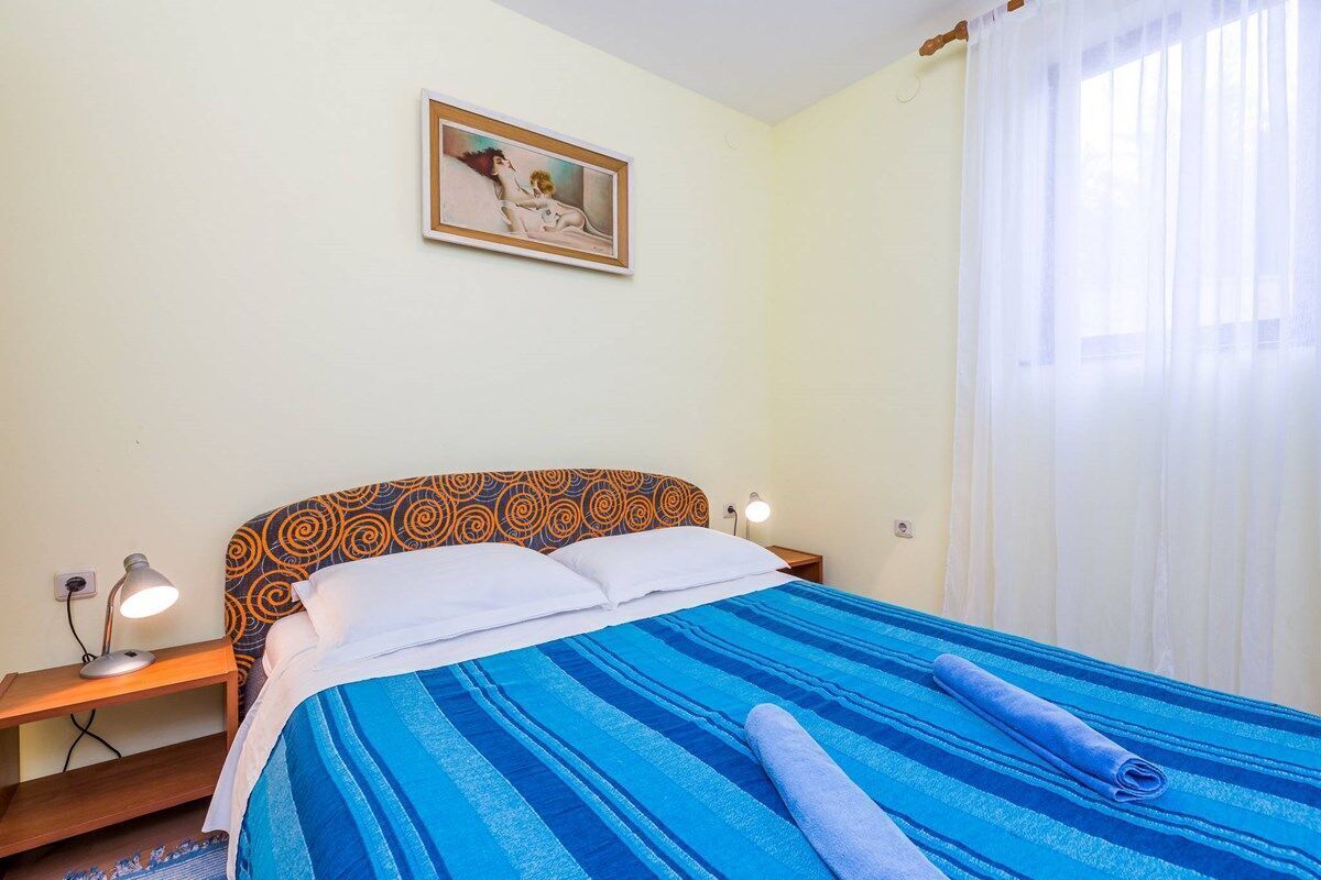 A bedroom with a bed, a bedside table, a lamp, a picture on the wall, and a window with curtains.