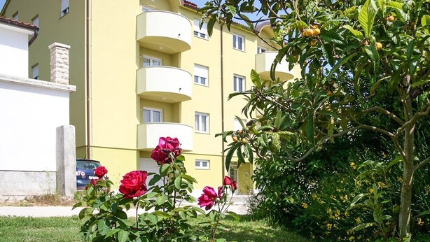 Ein mehrstöckiges Gebäude mit Balkonen, umgeben von Grünflächen und Blumen.