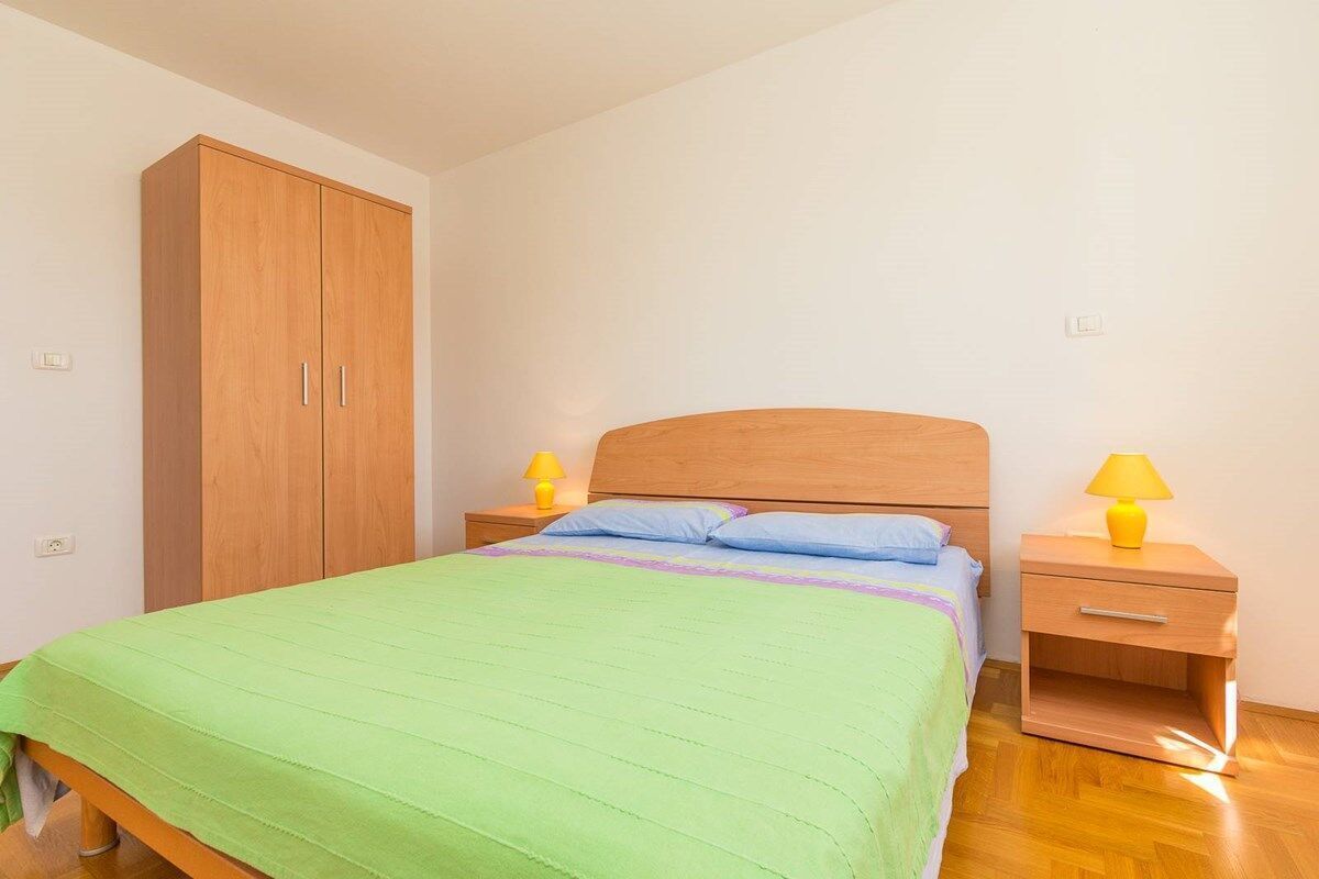 A bedroom with a bed, two bedside tables with lamps, a wooden wardrobe, and a nightstand.
