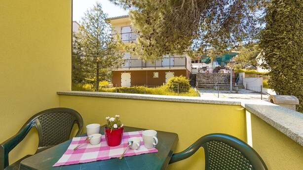 A balcony with a table set for two, chairs, and a view of a building with balconies. - Apartments Verde (16211-A2) - Premantura (Premantura)