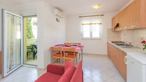 A compact kitchen with wooden cabinets, a dining table with chairs, and a red sofa. - Apartments Verde (16211-A2) - Premantura (Premantura)