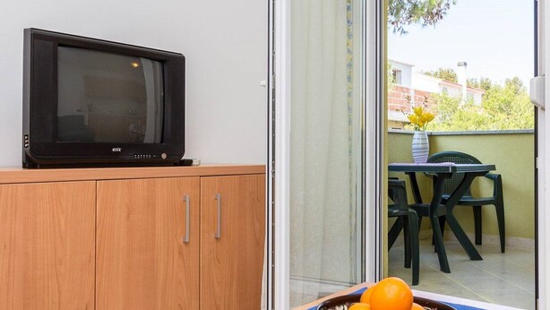 Un televisor sobre un mueble de madera, una mesa con sillas y un bol de naranjas.