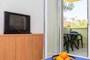 Een televisie op een houten kast, een tafel met stoelen en een schaal met mandarijnen.
