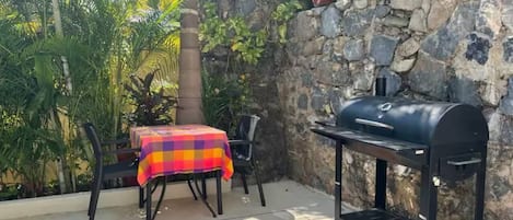 An outdoor patio with a barbecue grill, a table with a colorful tablecloth, and potted plants.