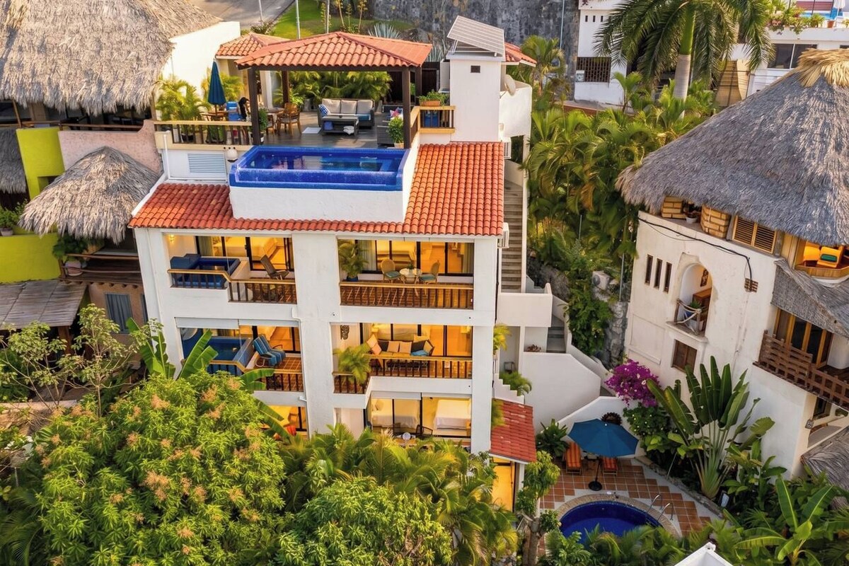 A multi-story hotel with a rooftop pool, balconies, and lush greenery.