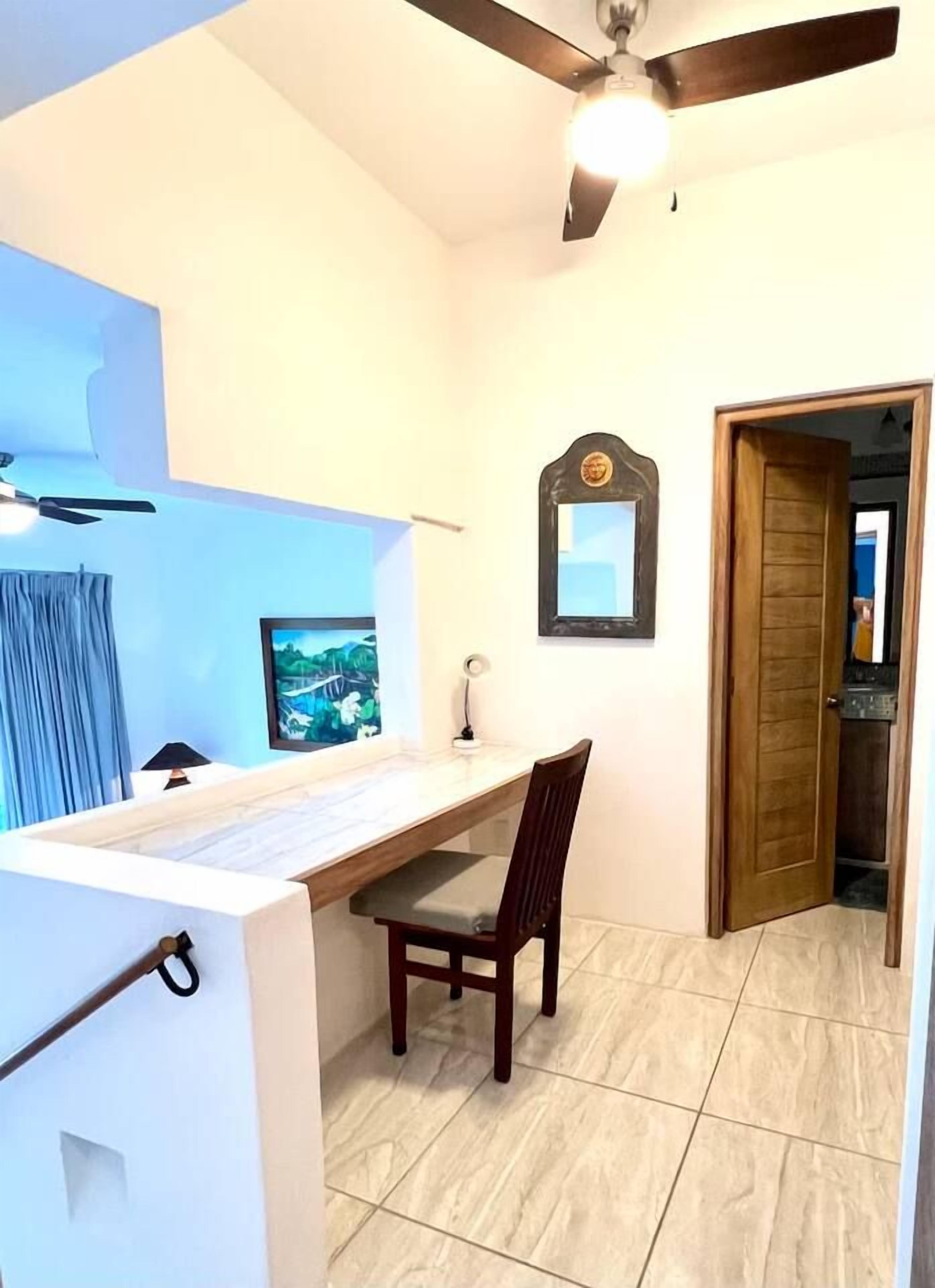 Habitación con escritorio, silla, ventilador de techo y puerta que da a otra habitación.