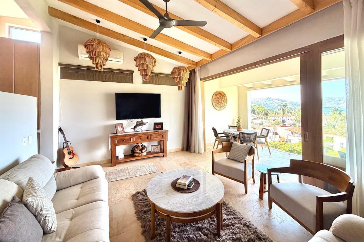 Een ruime woonkamer met een plafondventilator, een televisie, een gitaar en een balkon met uitzicht.