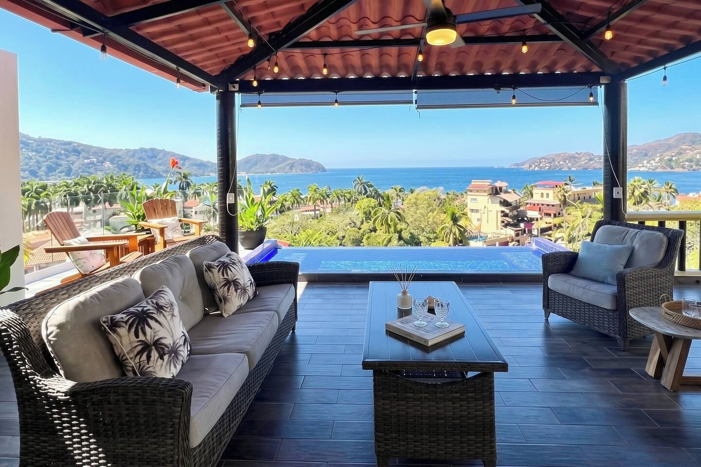 A covered outdoor seating area with a view of the ocean and hills.