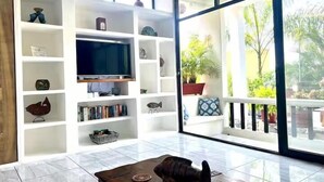 Un salón con televisor, estanterías y vistas a un jardín a través de grandes puertas correderas.