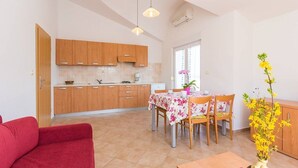 A modern kitchen with wooden cabinets, a dining table with chairs, and a red sofa. - Apartments Verde (16211-A5) - Premantura (Premantura)