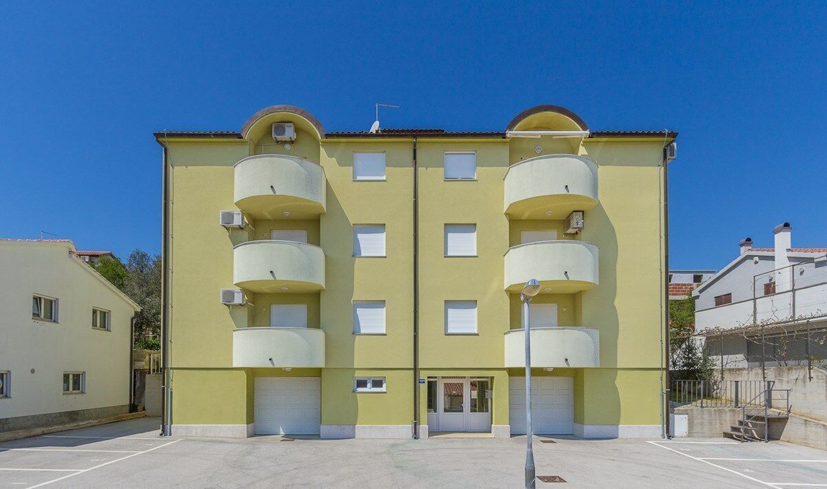 A yellow multi-story building with balconies, a garage door, and a clear sky.