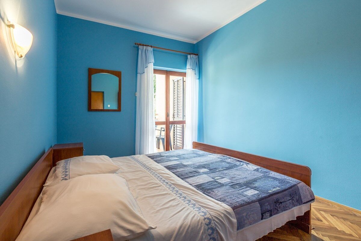 Una camera da letto con un letto in legno, un comodino, uno specchio fissato alla parete e una finestra con tende.
