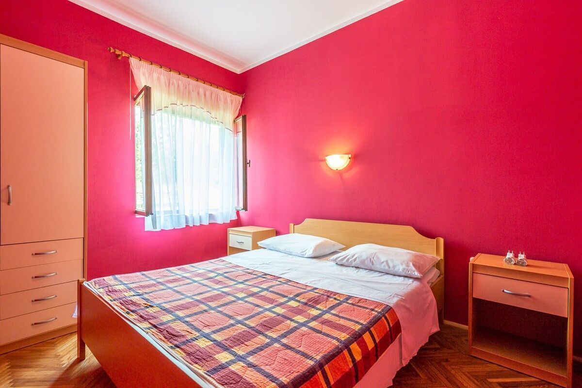 A bedroom with a bed, a nightstand, a wardrobe, and a window with curtains.