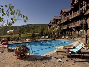 Un espace piscine avec des chaises longues, un arrangement floral et un bâtiment doté de balcons.