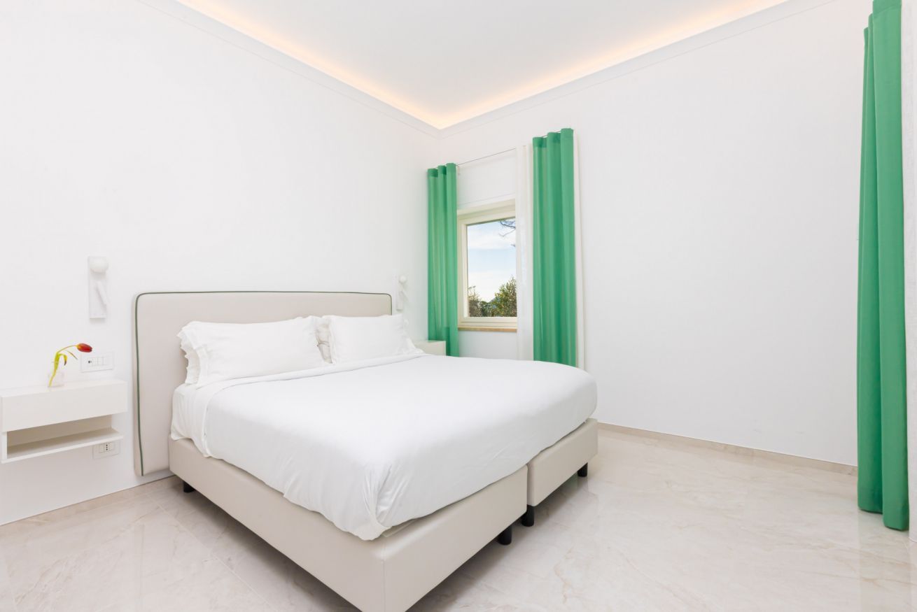 A modern bedroom with a bed, a nightstand, and a window with green curtains.