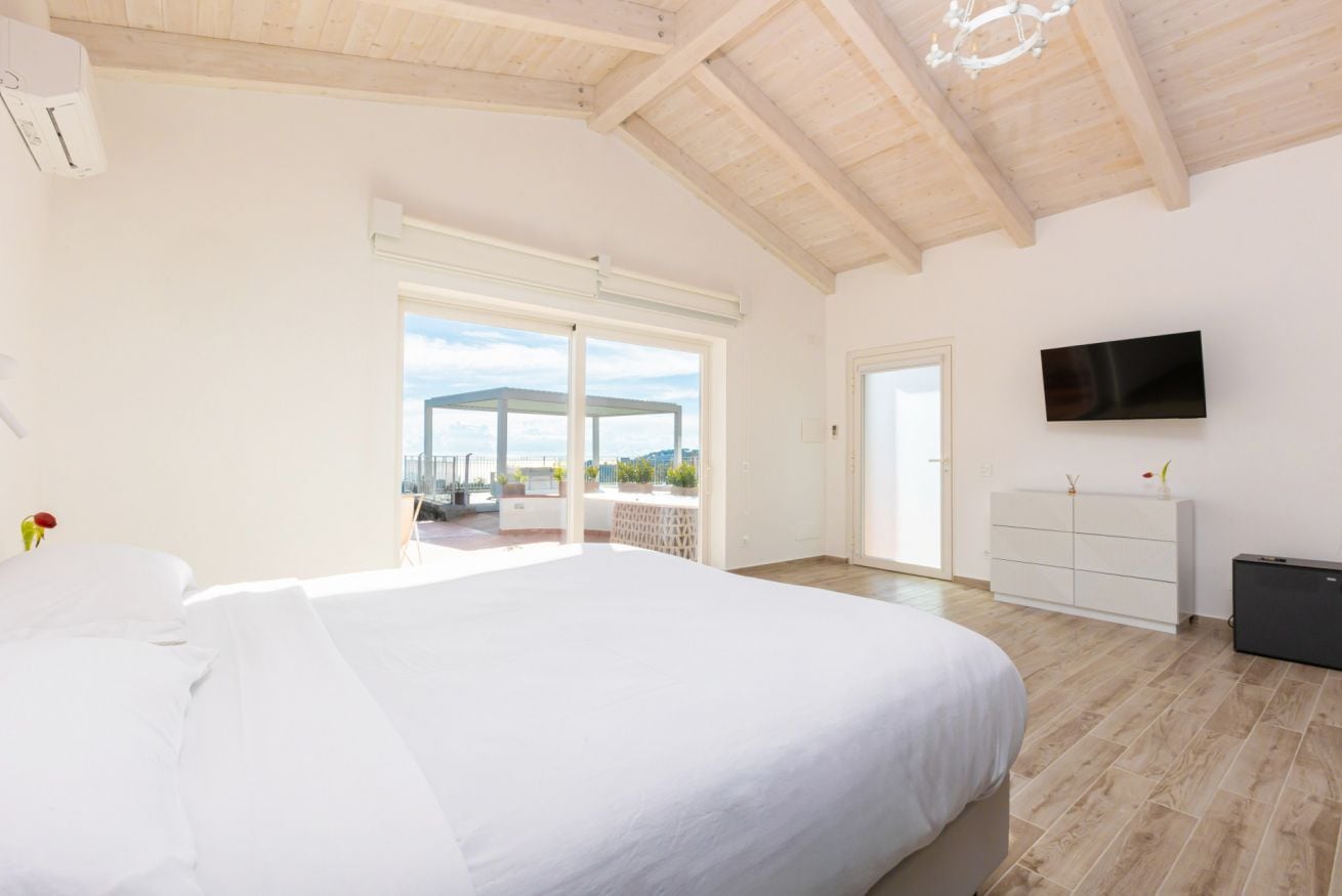 A spacious bedroom with a large bed, a television mounted on the wall, and a sliding glass door leading to an outdoor area.