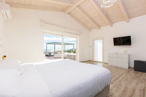 Een ruime slaapkamer met een groot bed, een aan de muur bevestigde televisie en een schuifdeur naar een buitenruimte.
