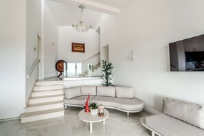 A modern living room with a curved sofa, a coffee table, and a staircase leading to an upper level. - Modern Sorrento Coast Villa with Private Pool & Terrace (Massa Lubrense)