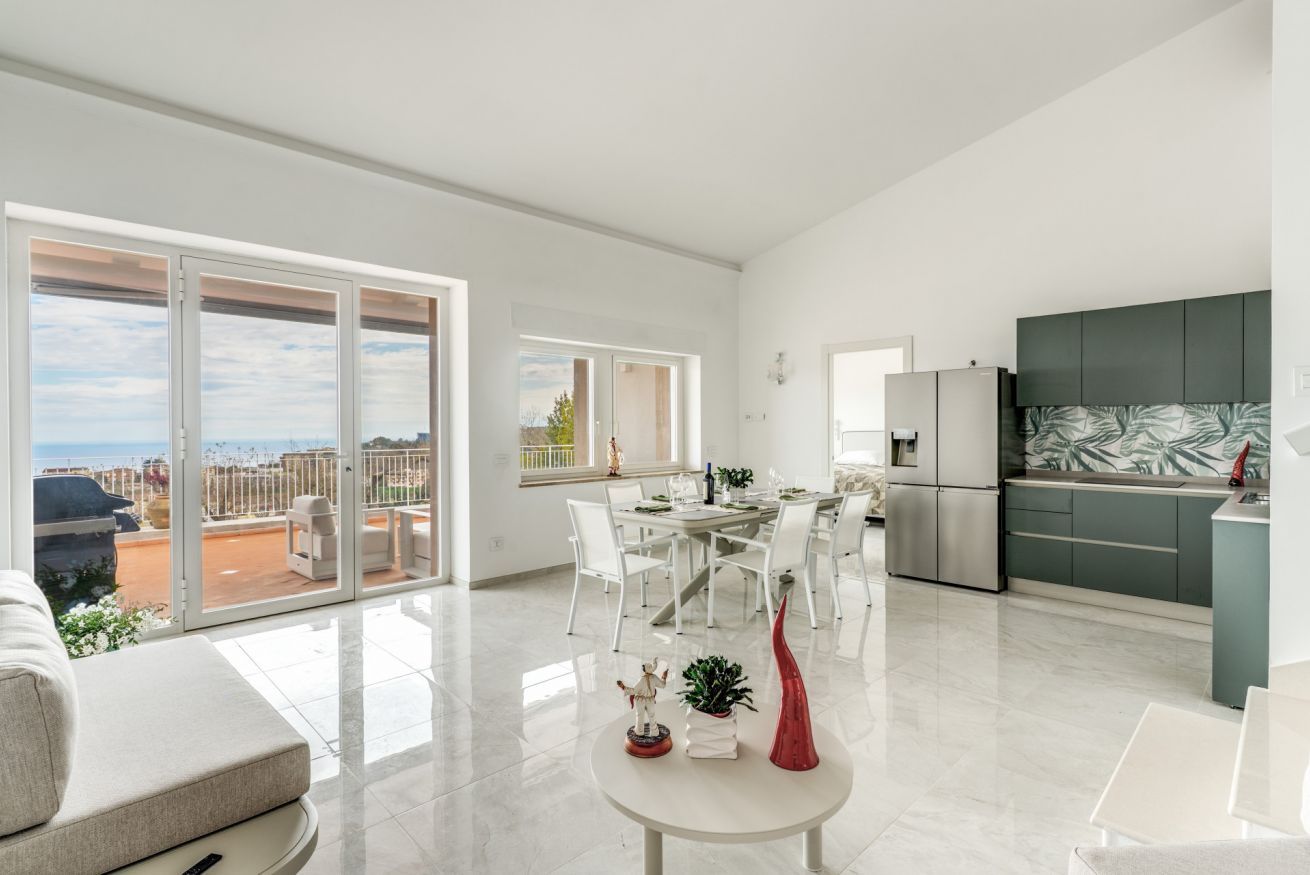 A modern apartment with a dining area, kitchen, and a balcony with a view.