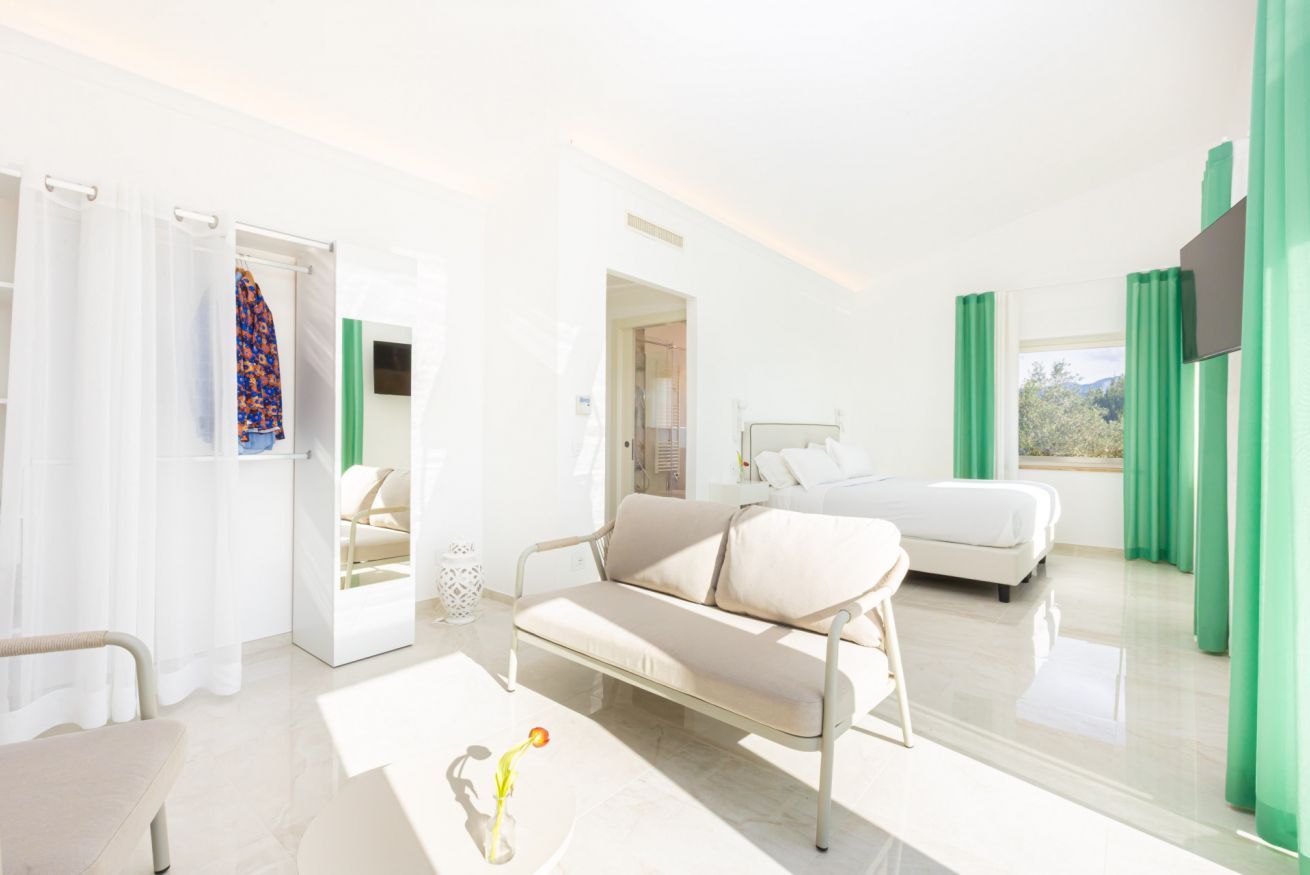 Quarto de hotel luminoso com sofá, cama, televisão e vista para o exterior.