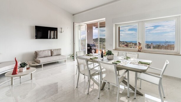 A modern living room with a dining area, a sofa, and a TV mounted on the wall. - Modern Sorrento Coast Villa with Private Pool & Terrace (Massa Lubrense)