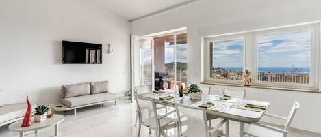 Una sala de estar moderna con comedor, un sofá y un televisor montado en la pared.