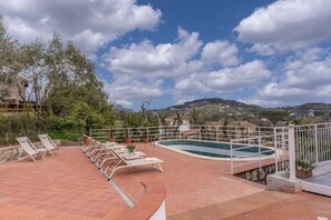 Un espace piscine aménagé sur le toit, avec des chaises longues et une piscine, entouré d’arbres et avec des collines en arrière-plan.