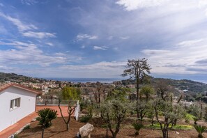 A residential area with a white building, trees, and a distant view of a town and coastline. - Modern Sorrento Coast Villa with Private Pool & Terrace (Massa Lubrense)