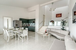 A modern living room with a dining area, a kitchen in the background, and a staircase leading to an upper floor. - Modern Sorrento Coast Villa with Private Pool & Terrace (Massa Lubrense)