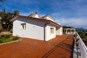 Une maison moderne à deux étages, dotée d’une terrasse en bois et d’un espace salon extérieur abrité.