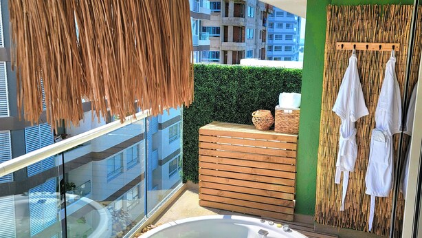 A balcony with a hot tub, a woven hanging chair, and a bamboo wall with towels. - Personal Jacuzzi•Beach •Pool•Personal Concierge (La Boquilla)