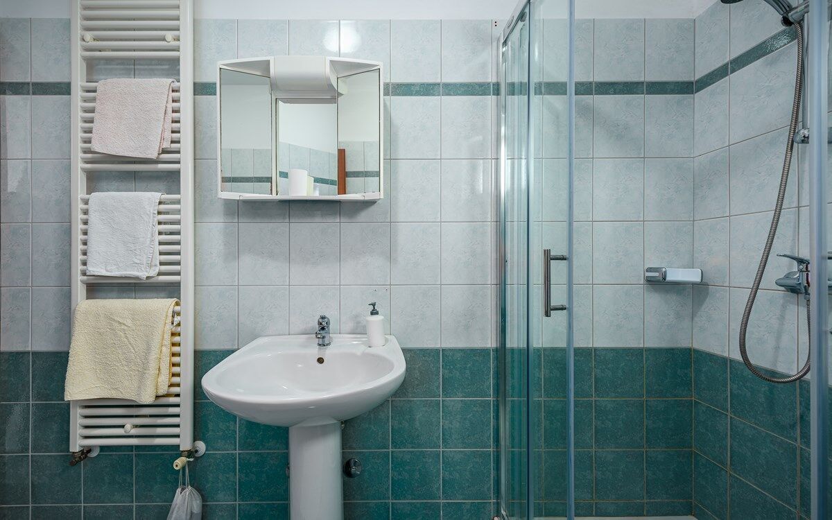Un baño con lavamanos, espejo, toallero y ducha.