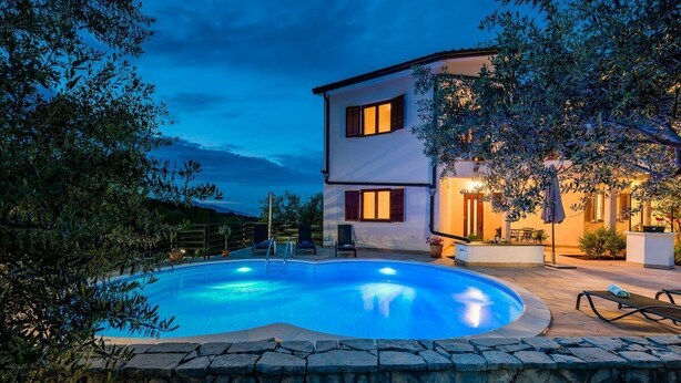 Uma casa de dois andares com piscina, muro de pedra e móveis de jardim.
