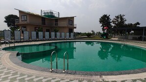 Una piscina de borde curvo, un área de descanso cubierta y un edificio con balcón.