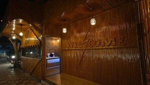 Fachada de madera con un cartel de 'WELCOME' y un banco frente al edificio.