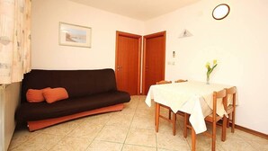 Ein Zimmer mit einem dunkelbraunen Sofa, einem Esstisch mit weißem Tischlein und zwei Holztüren.
