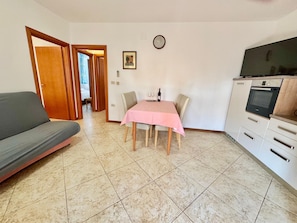 A living room with a sofa, a dining table with a pink tablecloth, and a kitchen area with cabinets and a TV. - Apartments Ladonia (16296-A2) - Krnica (Pula) (Krnica (Pula))