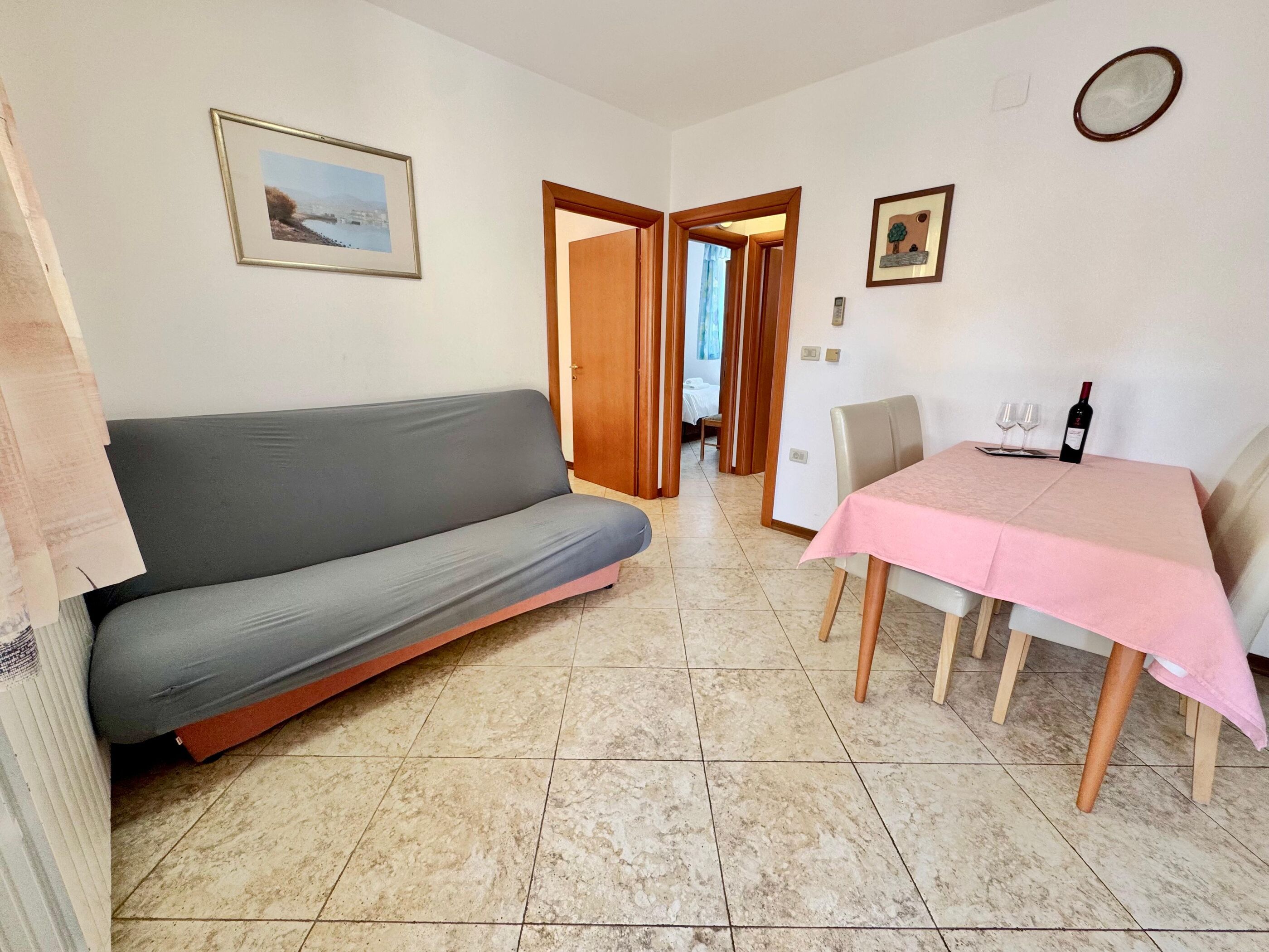 Una habitación con sofá, una mesa de comedor con mantel rosa y una cama al fondo.